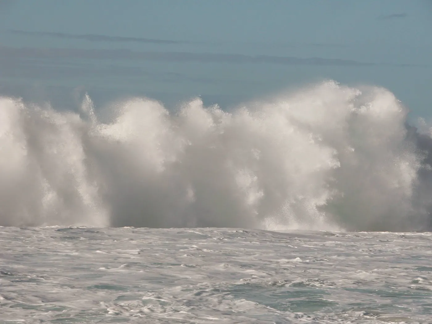 A massive wave breaking, white spray towering over churning sea